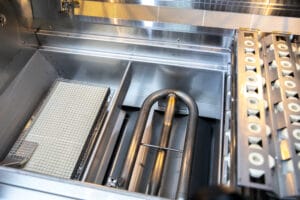 Interior view of an industrial machine with conveyor parts and a metal grid basket, likely used for manufacturing or processing operations.