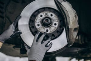 A person wearing protective gloves is servicing a car's disc brake system.